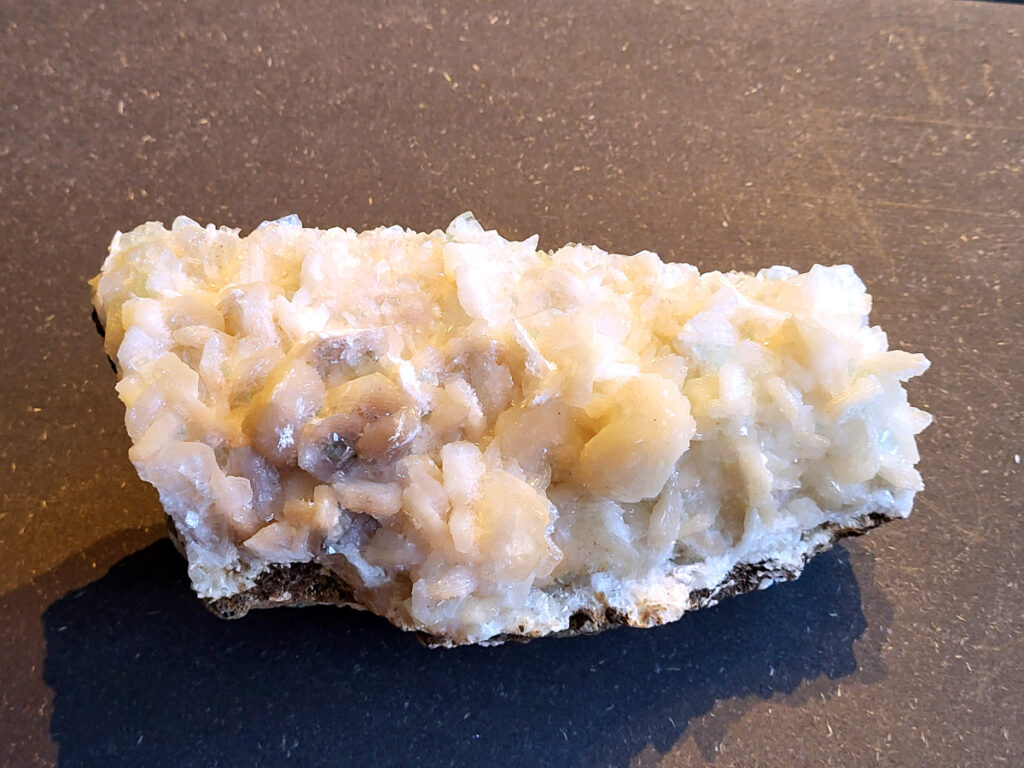 <strong>Stilbiet Cluster, 1,2 kg, 23,- euro, nr. 5</strong>

Stilbiet,
<strong>De waaier- of bundelvormige kristallen met een zijdeachtige glans en soms lichtgroen-geelatige gloed zijn typisch voor stilbiet.</strong>
De helder witte tot doorschijnende kubusvormige kristallen aan de basis zijn apofyliet.
De gele of groenige zweem kan komen van een lichte epidoot- of prehniet-insluiting, of een natuurlijke oxidatie aan het oppervlak.
Energetische werking:
<strong>Stilbiet opent het hart en helpt loslaten van zorgen; het is zacht, troostend en bevordert vertrouwen in de loop van het leven.</strong>
Apofyliet versterkt intuïtie, helderheid en spirituele verbinding — een “lichtbrenger” die energie zuivert in een ruimte.
Samen vormen ze een kalmerende, hoogtrillende combinatie die ideaal is voor meditatie, healingruimtes of slaapkamers (voor rust en inzicht).
Zorgtip:
Houd ze uit direct zonlicht (kan verkleuren) en reinig liever met klank, maanlicht of wierook in plaats van water — apofyliet lost iets op bij langdurig vocht.
<strong> Uiterlijk:</strong>
De perzik- tot crème-witte kleur,
De glanzende, waaier- of bloemvormige kristalstructuur,
De zachte, zijdeachtige glans (bijna parelmoerachtig),
al die kenmerken passen heel goed bij stilbiet.
De ronde, lichtgrijze korrelige bol bovenop kan een heulandiet- of chalcedoon-vorming zijn die samen met de stilbiet is gegroeid.
Energetische betekenis:
<strong>Stilbiet hoort bij het hart en het kruinchakra — een zachte, troostende energie die helpt bij het loslaten van oude patronen en het verbinden met hogere leiding.
Ze ondersteunt intuïtie, dromen en zachtheid in relaties — een heel liefdevolle steen om in huis te hebben, vooral bij healing- of slaapruimtes.</strong>