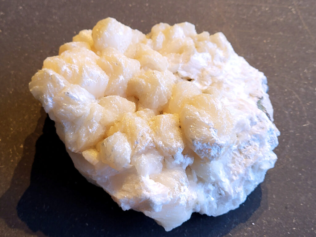 <strong>Stilbiet Cluster, 1,8kg, 35,- euro, nr. 6</strong>

Stilbiet,
<strong>De waaier- of bundelvormige kristallen met een zijdeachtige glans en soms lichtgroen-geelatige gloed zijn typisch voor stilbiet.</strong>
De helder witte tot doorschijnende kubusvormige kristallen aan de basis zijn apofyliet.
De gele of groenige zweem kan komen van een lichte epidoot- of prehniet-insluiting, of een natuurlijke oxidatie aan het oppervlak.
Energetische werking:
<strong>Stilbiet opent het hart en helpt loslaten van zorgen; het is zacht, troostend en bevordert vertrouwen in de loop van het leven.</strong>
Apofyliet versterkt intuïtie, helderheid en spirituele verbinding — een “lichtbrenger” die energie zuivert in een ruimte.
Samen vormen ze een kalmerende, hoogtrillende combinatie die ideaal is voor meditatie, healingruimtes of slaapkamers (voor rust en inzicht).
Zorgtip:
Houd ze uit direct zonlicht (kan verkleuren) en reinig liever met klank, maanlicht of wierook in plaats van water — apofyliet lost iets op bij langdurig vocht.
<strong> Uiterlijk:</strong>
De perzik- tot crème-witte kleur,
De glanzende, waaier- of bloemvormige kristalstructuur,
De zachte, zijdeachtige glans (bijna parelmoerachtig),
al die kenmerken passen heel goed bij stilbiet.
De ronde, lichtgrijze korrelige bol bovenop kan een heulandiet- of chalcedoon-vorming zijn die samen met de stilbiet is gegroeid.
<strong>Energetische betekenis:
Stilbiet hoort bij het hart en het kruinchakra — een zachte, troostende energie die helpt bij het loslaten van oude patronen en het verbinden met hogere leiding.
Ze ondersteunt intuïtie, dromen en zachtheid in relaties — een heel liefdevolle steen om in huis te hebben, vooral bij healing- of slaapruimtes.</strong>