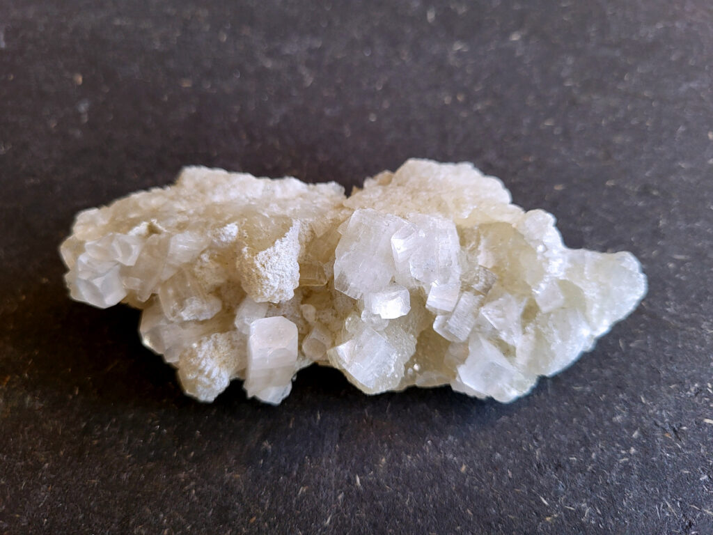 Apofyliet, doorsnee 11 cm, 150 gr. 7,- euro

Apofyliet op matrix, beschrijving

apofyliet op matrix
De doorzichtige tot melkachtige blokvormige kristallen zijn typisch voor apofyliet.
Apofyliet vormt vaak vierkante of rechthoekige kristallen met vlakke toppen.
De groenige korrelige ondergrond is een zeolietmatrix (bijvoorbeeld stilbiet of heulandiet).
Dit soort combinaties komt vaak uit India (Maharashtra regio).
Kenmerken van apofyliet
Kleur: transparant, wit, soms lichtgroen
Kristalvorm: kubusachtig / blokvormig met glanzende vlakken
Glans: glasachtig
Vaak gevonden samen met: stilbiet, heulandiet, calciet
Apofyliet is een helder of wit mineraal dat behoort tot de groep van de calciumsilicaten. Het wordt voornamelijk gevonden in vulkanische gesteenten, vooral in de buurt van breuken en scheuren. In de spirituele wereld wordt Apofyliet beschouwd als een krachtige steen met een hoge vibratie die helpt bij het openen en activeren van de hogere chakra's, met name het derde oog en de kruinchakra.
Apofyliet werkt ondersteunend bij innerlijke druk en angsten, tevens goede steen om fixaties en rigiditeit los te laten. De steen spoort je aan om je thuis te voelen in je eigen lichaam. Dit maakt het een zeer goede steen voor meditatieve doeleinden. De energie van Apofyliet wordt ook geassocieerd met helderheid, zuiverheid en zuivering. Het kan worden gebruikt om negatieve energieën en emoties te verwijderen en om een gevoel van kalmte en vrede te bevorderen. Het kan ook helpen bij het verminderen van stress en angst en het bevorderen van innerlijke rust en harmonie.
Fysiek wordt Apofyliet geassocieerd met het versterken van het immuunsysteem en het bevorderen van een gezonde spijsvertering. Het kan ook worden gebruikt om hoofdpijn, migraine en andere pijnlijke aandoeningen te verlichten. Het loslaten van fixaties en rigiditeit kan ook verlichting bieden voor fysieke spanning in het lichaam.
Over het algemeen wordt Apofyliet beschouwd als een krachtige steen voor spirituele groei en genezing, en het kan een waardevolle aanvulling zijn op meditatie- en genezingspraktijken. Het biedt emotionele en mentale ondersteuning door het helpen loslaten van fixaties en rigiditeit, en het bevorderen van innerlijke rust en harmonie. Het biedt ook fysieke voordelen, zoals het versterken van het immuunsysteem en het verlichten van hoofdpijn en andere pijnlijke aandoeningen.


