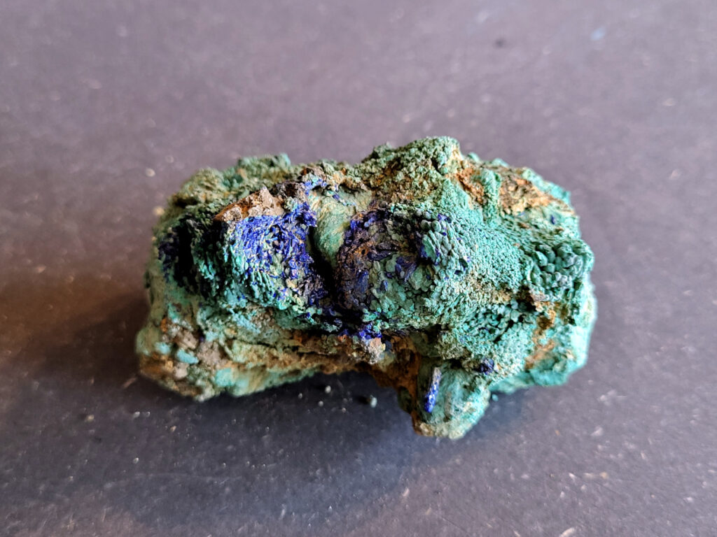 <strong>Azuriet met Malachiet, 290 gram, 5cm hoog, 9cm breed, 22,- euro, nr. 6

Azuriet op Malachiet
Azuriet op Malachiet op een ijzerrijke steen.
Azuriet heeft een diep blauwe kleur en wordt vaak gevonden in deze combinatie.
De groene stukjes zijn malachiet, een mineraal dat ontstaat waar koper in de grond zit. De bruine steen eromheen is waarschijnlijk roestachtig gesteente met ijzer.
Malachiet kan soms fel groen en korrelig groeien in kleine plekjes of holtes.
Bruine steen met groene malachiet (kopermineraal) en Azuriet.
</strong>