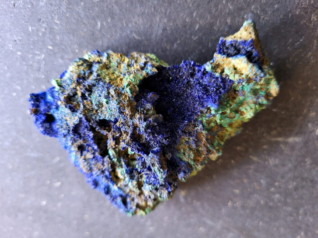 <strong>Azuriet op Malachiet, 152 gram, 7cm hoog, 11cm breed, 11,- euro, nr. 3

Azuriet op Malachiet
Azuriet op Malachiet op een ijzerrijke steen.
Azuriet heeft een diep blauwe kleur en wordt vaak gevonden in deze combinatie.
De groene stukjes zijn malachiet, een mineraal dat ontstaat waar koper in de grond zit. De bruine steen eromheen is waarschijnlijk roestachtig gesteente met ijzer.
Malachiet kan soms fel groen en korrelig groeien in kleine plekjes of holtes.
Bruine steen met groene malachiet (kopermineraal) en Azuriet.
</strong>