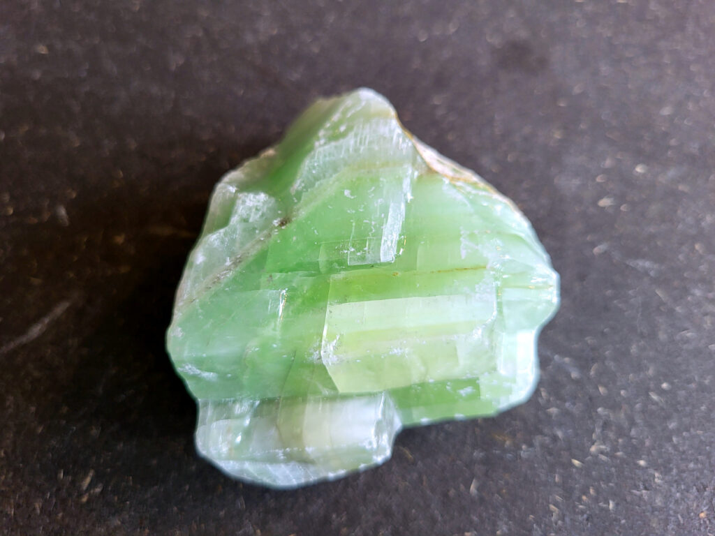 Groene Calciet, 250 gram, 6,50 euro, nr. 4

Calciet, 
Calciet is een veelvoorkomend mineraal dat voornamelijk bestaat uit calciumcarbonaat. Het komt in diverse kleuren en vormen voor en wordt in veel industrieën gebruikt, maar ook in de esoterie.
Algemene kenmerken:
Samenstelling: Calciet bestaat voornamelijk uit calciumcarbonaat (CaCO3).
Vorming: Het ontstaat door afzetting van calciumcarbonaat in water, maar ook door ophoping van schelpen en skeletten van zeedieren.
Uiterlijk: Het heeft vaak een glasachtige glans, is doorzichtig tot doorschijnend en kan vele kleuren hebben, zoals geel, oranje, rood, bruin, blauw, groen, roze, wit en kleurloos.
Hardheid: Calciet heeft een hardheid van 3 op de schaal van Mohs.
Veelvoorkomend: Het is een van de meest voorkomende mineralen en is een hoofdbestanddeel van kalksteen, marmer en krijt.
Esoterie:
In de edelsteentherapie wordt calciet gezien als een steen die energie versterkt, negatieve energieën verwijdert en spirituele groei bevordert. Verschillende kleuren calciet hebben specifieke eigenschappen, zoals gele calciet voor doorzettingsvermogen en moed, en mangano calciet voor emotionele heling.
Specifieke calcietsoorten:
Gele Calciet: Staat bekend om het absorberen van negativiteit, het versterken van doorzettingsvermogen en het aantrekken van succes.
Blauwe Calciet: Wordt geassocieerd met kalmering, communicatie en het loslaten van stress.
Groene Calciet: Werkt op de hartchakra, bevordert liefde, compassie en emotionele heling.
Mangano Calciet: Wordt gebruikt voor emotionele heling, het loslaten van oud verdriet en het versterken van zelfvertrouwen.
Reiniging:
Calciet kan op verschillende manieren gereinigd worden, maar het is belangrijk om te weten dat sommige soorten, zoals gele calciet, niet goed tegen water kunnen.
Andere reinigingsmethoden zijn bijvoorbeeld reinigen met edelstenenspray, op een Amethist of bergkristal leggen, of reinigen met selenite.
Het is een steen die kan worden gebruikt voor energieversterking, emotionele heling en het bevorderen van spirituele groei, afhankelijk van de specifieke kleur en eigenschappen.