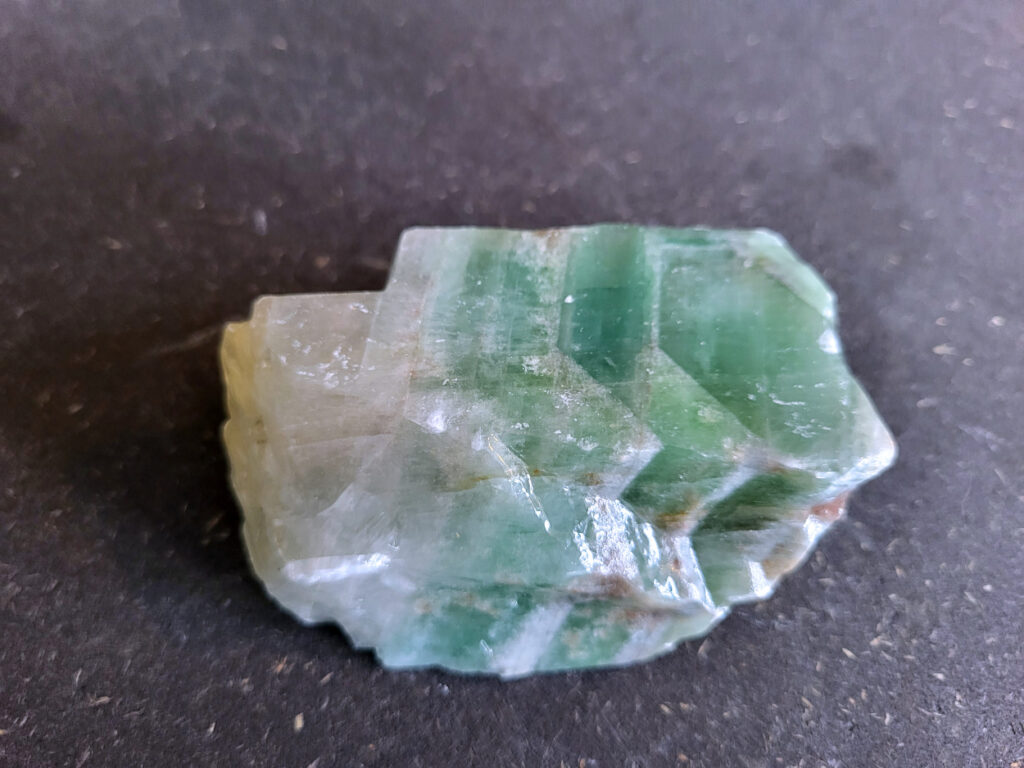 Groene Calciet, 270 gram, 7,- euro, nr. 2

Calciet, 
Calciet is een veelvoorkomend mineraal dat voornamelijk bestaat uit calciumcarbonaat. Het komt in diverse kleuren en vormen voor en wordt in veel industrieën gebruikt, maar ook in de esoterie.
Algemene kenmerken:
Samenstelling: Calciet bestaat voornamelijk uit calciumcarbonaat (CaCO3).
Vorming: Het ontstaat door afzetting van calciumcarbonaat in water, maar ook door ophoping van schelpen en skeletten van zeedieren.
Uiterlijk: Het heeft vaak een glasachtige glans, is doorzichtig tot doorschijnend en kan vele kleuren hebben, zoals geel, oranje, rood, bruin, blauw, groen, roze, wit en kleurloos.
Hardheid: Calciet heeft een hardheid van 3 op de schaal van Mohs.
Veelvoorkomend: Het is een van de meest voorkomende mineralen en is een hoofdbestanddeel van kalksteen, marmer en krijt.
Esoterie:
In de edelsteentherapie wordt calciet gezien als een steen die energie versterkt, negatieve energieën verwijdert en spirituele groei bevordert. Verschillende kleuren calciet hebben specifieke eigenschappen, zoals gele calciet voor doorzettingsvermogen en moed, en mangano calciet voor emotionele heling.
Specifieke calcietsoorten:
Gele Calciet: Staat bekend om het absorberen van negativiteit, het versterken van doorzettingsvermogen en het aantrekken van succes.
Blauwe Calciet: Wordt geassocieerd met kalmering, communicatie en het loslaten van stress.
Groene Calciet: Werkt op de hartchakra, bevordert liefde, compassie en emotionele heling.
Mangano Calciet: Wordt gebruikt voor emotionele heling, het loslaten van oud verdriet en het versterken van zelfvertrouwen.
Reiniging:
Calciet kan op verschillende manieren gereinigd worden, maar het is belangrijk om te weten dat sommige soorten, zoals gele calciet, niet goed tegen water kunnen.
Andere reinigingsmethoden zijn bijvoorbeeld reinigen met edelstenenspray, op een Amethist of bergkristal leggen, of reinigen met selenite.
Het is een steen die kan worden gebruikt voor energieversterking, emotionele heling en het bevorderen van spirituele groei, afhankelijk van de specifieke kleur en eigenschappen.