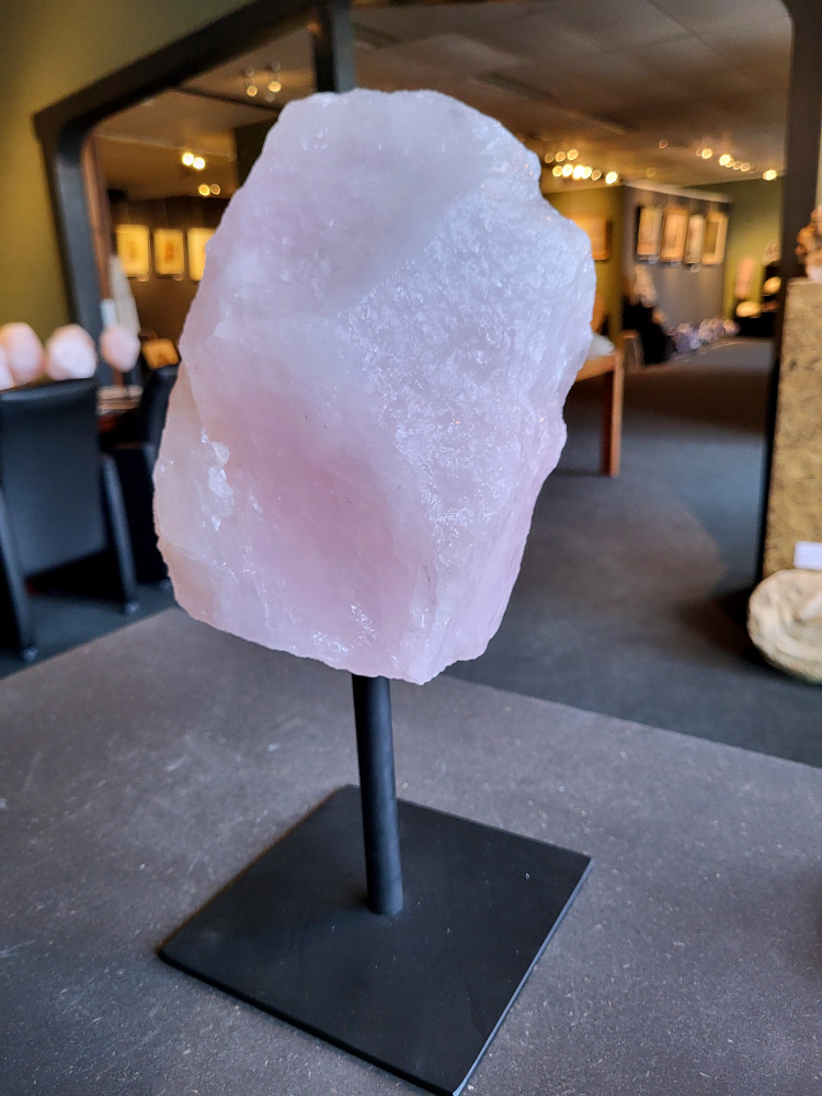 Rozenkwarts op standaard, 5,8kg, 70,- euro, nr. 26

Rozenkwarts, beschrijving
Rozenkwarts is een roze variëteit van kwarts, bekend om zijn zachte, liefdevolle energie en wordt vaak geassocieerd met het hartchakra.
Kenmerken:
Rozenkwarts varieert in kleur van lichtroze tot diep roze, vaak met een doorschijnende of troebele textuur.
Het is een mineraal dat voornamelijk bestaat uit siliciumdioxide, met sporen van titanium, ijzer of mangaan die de roze kleur veroorzaken.
Herkomst:
Rozenkwarts wordt op veel plaatsen in de wereld gevonden, waaronder Brazilië, Madagaskar, Rusland, India en de VS, maar de kwaliteit kan variëren.
Eigenschappen en Betekenis:

Rozenkwarts staat bekend als de "steen van de liefde" en wordt geassocieerd met het openen van het hartchakra, het bevorderen van zelfliefde, vergeving, compassie en het aantrekken van liefdevolle relaties.
Bescherming:
In sommige overtuigingen wordt rozenkwarts ook gebruikt voor bescherming en het afweren van negatieve energieën.
Verzorging:
Rozenkwarts kan het beste niet langdurig aan direct zonlicht worden blootgesteld, omdat de kleur kan vervagen.