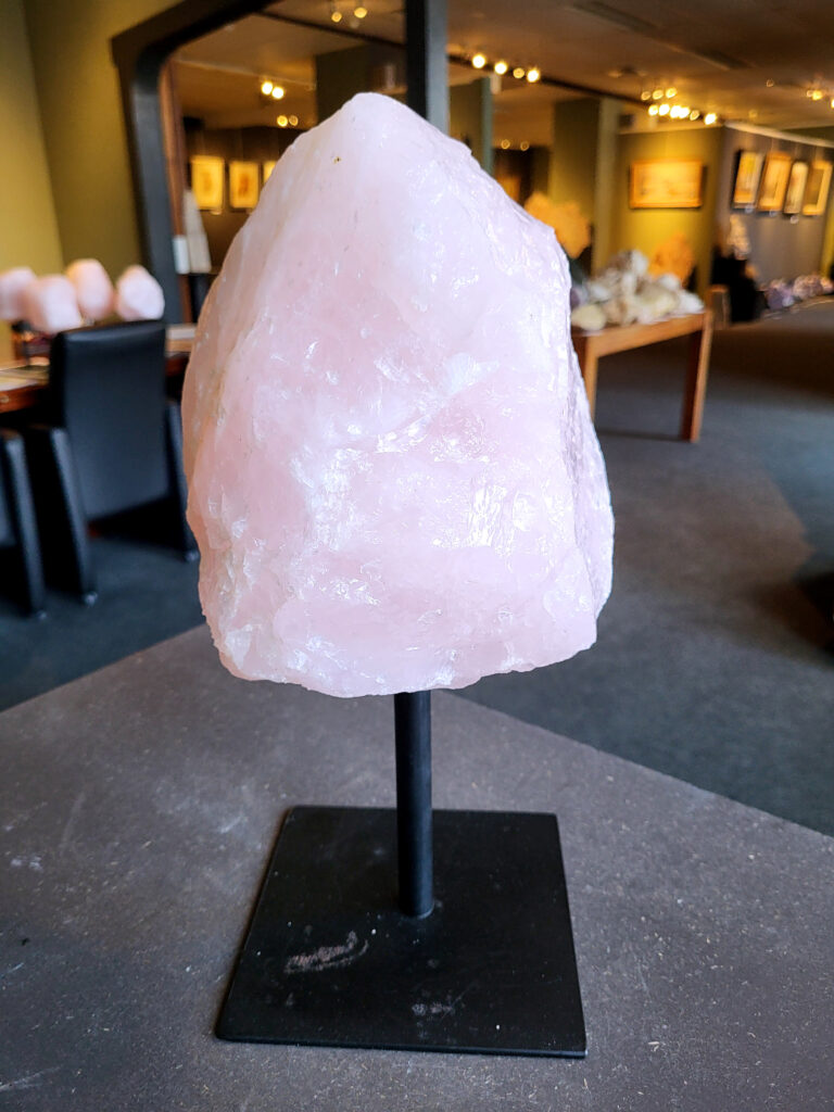 Rozenkwarts op standaard, 7,2kg, 88,- euro, nr. 25

Rozenkwarts, beschrijving
Rozenkwarts is een roze variëteit van kwarts, bekend om zijn zachte, liefdevolle energie en wordt vaak geassocieerd met het hartchakra.
Kenmerken:
Rozenkwarts varieert in kleur van lichtroze tot diep roze, vaak met een doorschijnende of troebele textuur.
Het is een mineraal dat voornamelijk bestaat uit siliciumdioxide, met sporen van titanium, ijzer of mangaan die de roze kleur veroorzaken.
Herkomst:
Rozenkwarts wordt op veel plaatsen in de wereld gevonden, waaronder Brazilië, Madagaskar, Rusland, India en de VS, maar de kwaliteit kan variëren.
Eigenschappen en Betekenis:

Rozenkwarts staat bekend als de "steen van de liefde" en wordt geassocieerd met het openen van het hartchakra, het bevorderen van zelfliefde, vergeving, compassie en het aantrekken van liefdevolle relaties.
Bescherming:
In sommige overtuigingen wordt rozenkwarts ook gebruikt voor bescherming en het afweren van negatieve energieën.
Verzorging:
Rozenkwarts kan het beste niet langdurig aan direct zonlicht worden blootgesteld, omdat de kleur kan vervagen.