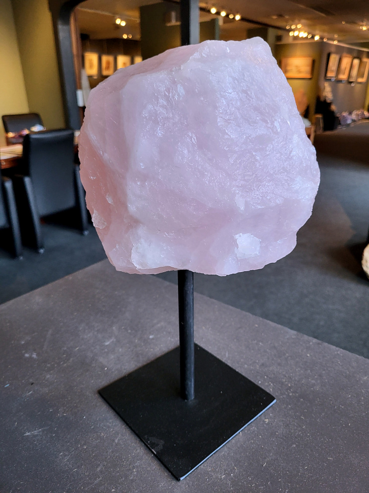 Rozenkwarts op standaard, 8,8kg, 105,- euro, nr. 22

Rozenkwarts, beschrijving
Rozenkwarts is een roze variëteit van kwarts, bekend om zijn zachte, liefdevolle energie en wordt vaak geassocieerd met het hartchakra.
Kenmerken:
Rozenkwarts varieert in kleur van lichtroze tot diep roze, vaak met een doorschijnende of troebele textuur.
Het is een mineraal dat voornamelijk bestaat uit siliciumdioxide, met sporen van titanium, ijzer of mangaan die de roze kleur veroorzaken.
Herkomst:
Rozenkwarts wordt op veel plaatsen in de wereld gevonden, waaronder Brazilië, Madagaskar, Rusland, India en de VS, maar de kwaliteit kan variëren.
Eigenschappen en Betekenis:

Rozenkwarts staat bekend als de "steen van de liefde" en wordt geassocieerd met het openen van het hartchakra, het bevorderen van zelfliefde, vergeving, compassie en het aantrekken van liefdevolle relaties.
Bescherming:
In sommige overtuigingen wordt rozenkwarts ook gebruikt voor bescherming en het afweren van negatieve energieën.
Verzorging:
Rozenkwarts kan het beste niet langdurig aan direct zonlicht worden blootgesteld, omdat de kleur kan vervagen.