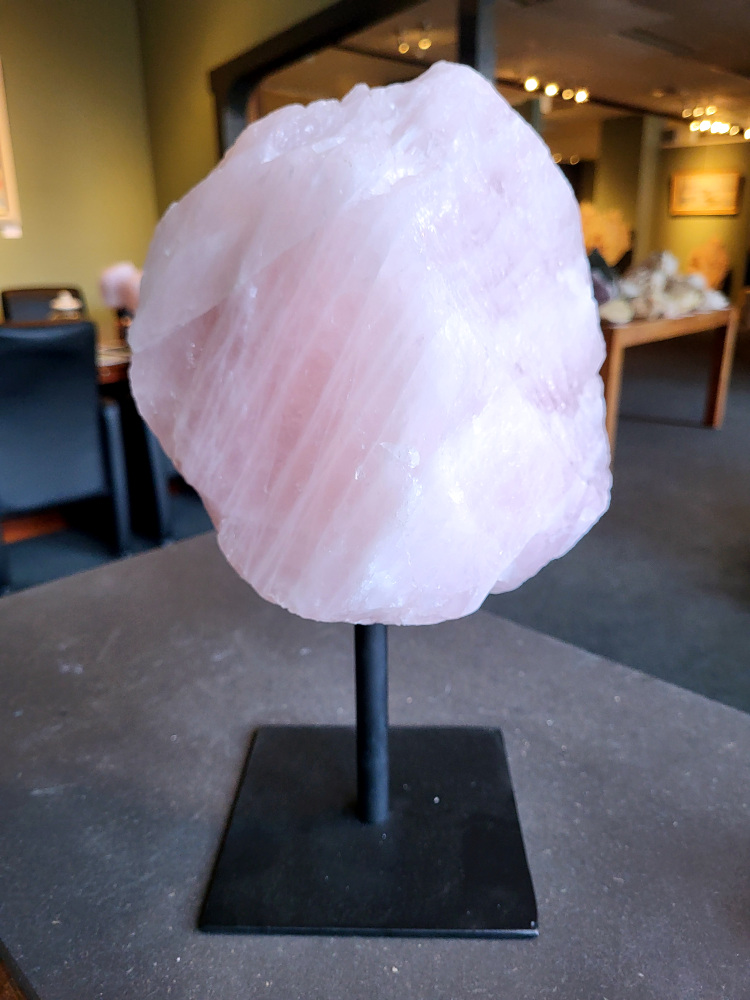 Rozenkwarts op standaard, 9,2kg, 110,- euro, nr. 21

Rozenkwarts, beschrijving
Rozenkwarts is een roze variëteit van kwarts, bekend om zijn zachte, liefdevolle energie en wordt vaak geassocieerd met het hartchakra.
Kenmerken:
Rozenkwarts varieert in kleur van lichtroze tot diep roze, vaak met een doorschijnende of troebele textuur.
Het is een mineraal dat voornamelijk bestaat uit siliciumdioxide, met sporen van titanium, ijzer of mangaan die de roze kleur veroorzaken.
Herkomst:
Rozenkwarts wordt op veel plaatsen in de wereld gevonden, waaronder Brazilië, Madagaskar, Rusland, India en de VS, maar de kwaliteit kan variëren.
Eigenschappen en Betekenis:

Rozenkwarts staat bekend als de "steen van de liefde" en wordt geassocieerd met het openen van het hartchakra, het bevorderen van zelfliefde, vergeving, compassie en het aantrekken van liefdevolle relaties.
Bescherming:
In sommige overtuigingen wordt rozenkwarts ook gebruikt voor bescherming en het afweren van negatieve energieën.
Verzorging:
Rozenkwarts kan het beste niet langdurig aan direct zonlicht worden blootgesteld, omdat de kleur kan vervagen.
