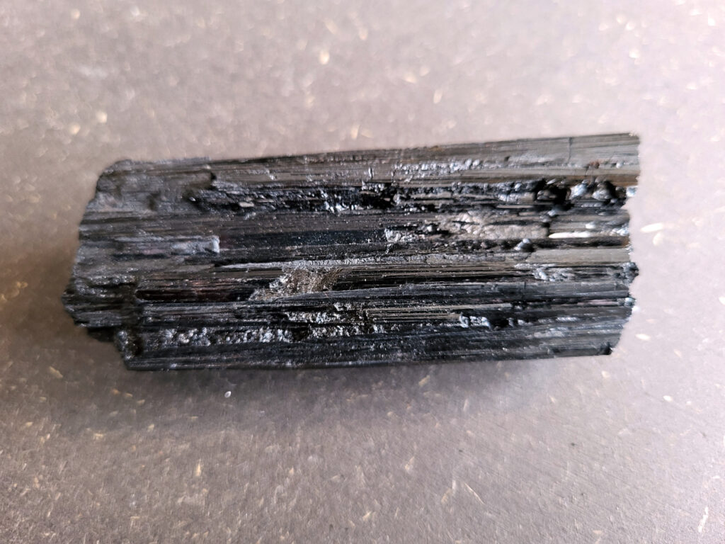 <strong>Toermalijn, zwarte toermalijn, 6,- euro, nr. 4

Zwarte toermalijn, beschrijving
Zwarte toermalijn (schorl) in een veldspaat-matrix.
Zwarte deel: zwarte toermalijn (schorl)
Bruin/roze gesteente eromheen: veldspaat (vaak kaliveldspaat uit pegmatiet)
Herkenningspunten
Zwart kristal met duidelijke lengtestrepen / lijnen
Vaak prismatisch (langwerpig kristal)
Zit vaak ingegroeid in veldspaat of granietachtige steen
Komt veel voor in pegmatietgesteente
Dit soort stukken ontstaan diep in de aarde wanneer magma langzaam afkoelt. In pegmatieten kunnen dan grote kristallen groeien, zoals:
Veldspaat, kwarts en toermalijn
Zwarte Toermalijn in Veldspaat
Zwarte toermalijn in veldspaat combineert de aardende en beschermende eigenschappen van zwarte toermalijn met de harmoniserende energieën van veldspaat. Deze unieke steen wordt gevormd wanneer zwarte toermalijnkristallen op natuurlijke wijze zijn ingebed in de veldspaatmatrix, waardoor een opvallend contrast ontstaat tussen de donkere toermalijn en de lichtere veldspaat.
Zwarte toermalijn staat bekend om zijn vermogen om negatieve energieën te absorberen en psychische bescherming te bieden. Het fungeert als een schild, buigt schadelijke energieën af en bevordert een gevoel van veiligheid en zekerheid. Met zijn aardende eigenschappen helpt zwarte toermalijn de drager te verankeren in de aarde, waardoor een gevoel van stabiliteit en evenwicht wordt bevorderd.
Veldspaat daarentegen is een steen van harmonie en integratie. Het bevordert een gevoel van eenheid en samenwerking, zowel binnen jezelf als in relaties met anderen. Veldspaat staat ook bekend om zijn kalmerende en verzachtende eigenschappen, waardoor stress en angst worden verlicht.
Samen creëert zwarte toermalijn in veldspaat een krachtige synergie van energieën. Het dient als een krachtig hulpmiddel voor spirituele bescherming en aarding, terwijl het ook innerlijke harmonie en emotioneel evenwicht bevordert. Deze steen kan bijzonder nuttig zijn voor degenen die een gevoel van stabiliteit en veiligheid in hun leven willen creëren, terwijl ze ook een diepere verbinding met de aarde en het spirituele rijk bevorderen.</strong>