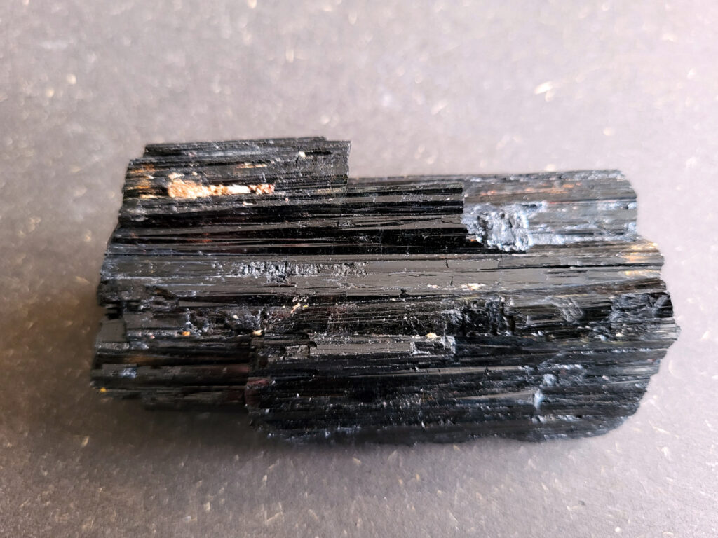 <strong>Toermalijn, zwarte toermalijn, 9,- euro, nr. 3

Zwarte toermalijn, beschrijving
Zwarte toermalijn (schorl) in een veldspaat-matrix.
Zwarte deel: zwarte toermalijn (schorl)
Bruin/roze gesteente eromheen: veldspaat (vaak kaliveldspaat uit pegmatiet)
Herkenningspunten
Zwart kristal met duidelijke lengtestrepen / lijnen
Vaak prismatisch (langwerpig kristal)
Zit vaak ingegroeid in veldspaat of granietachtige steen
Komt veel voor in pegmatietgesteente
Dit soort stukken ontstaan diep in de aarde wanneer magma langzaam afkoelt. In pegmatieten kunnen dan grote kristallen groeien, zoals:
Veldspaat, kwarts en toermalijn
Zwarte Toermalijn in Veldspaat
Zwarte toermalijn in veldspaat combineert de aardende en beschermende eigenschappen van zwarte toermalijn met de harmoniserende energieën van veldspaat. Deze unieke steen wordt gevormd wanneer zwarte toermalijnkristallen op natuurlijke wijze zijn ingebed in de veldspaatmatrix, waardoor een opvallend contrast ontstaat tussen de donkere toermalijn en de lichtere veldspaat.
Zwarte toermalijn staat bekend om zijn vermogen om negatieve energieën te absorberen en psychische bescherming te bieden. Het fungeert als een schild, buigt schadelijke energieën af en bevordert een gevoel van veiligheid en zekerheid. Met zijn aardende eigenschappen helpt zwarte toermalijn de drager te verankeren in de aarde, waardoor een gevoel van stabiliteit en evenwicht wordt bevorderd.
Veldspaat daarentegen is een steen van harmonie en integratie. Het bevordert een gevoel van eenheid en samenwerking, zowel binnen jezelf als in relaties met anderen. Veldspaat staat ook bekend om zijn kalmerende en verzachtende eigenschappen, waardoor stress en angst worden verlicht.
Samen creëert zwarte toermalijn in veldspaat een krachtige synergie van energieën. Het dient als een krachtig hulpmiddel voor spirituele bescherming en aarding, terwijl het ook innerlijke harmonie en emotioneel evenwicht bevordert. Deze steen kan bijzonder nuttig zijn voor degenen die een gevoel van stabiliteit en veiligheid in hun leven willen creëren, terwijl ze ook een diepere verbinding met de aarde en het spirituele rijk bevorderen.</strong>