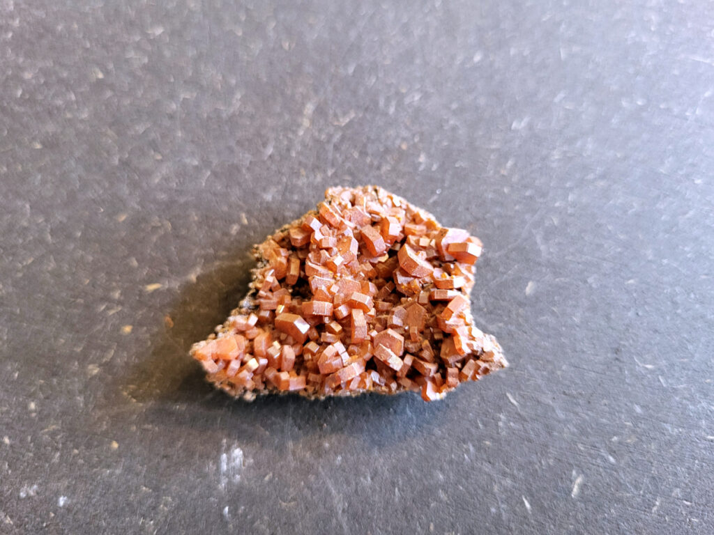 <strong>Vanadiniet, 28 gram, 4cm doorsnee, 8,- euro, nr. 109</strong>

<strong>Vanadiniet, beschrijving,

Vanadiniet is een mineraal behorend tot de groep van chlooride mineralen van lood (Pb₅(VO₄)₃Cl). Het staat bekend om zijn dieprode tot oranjerode    kristallen, vaak hexagonaal van vorm. Vanadiniet ontstaat meestal in de     oxidatiezone van loodertsen, en het wordt soms verzameld vanwege zijn spectaculaire kristalvorm en kleur. Vanadiniet kan ook geringe hoeveelheden bariet en andere achtergrondmineralen bevatten. Het heeft een hoge           densiteit en een glasachtige glans.

Associatie van Vanadiniet met Bariet
In de minerologie komt vanadiniet vaak voor op of samen met bariet, 
omdat beide mineralen zich kunnen vormen in de oxidatiezone van 
loodaders. Deze combinatie wordt soms door verzamelaars gezocht omdat de contrasterende kleuren en kristalvormen esthetisch aantrekkelijk zijn: de rode kristallen van vanadiniet op een witte of lichtgekleurde barietbasis. Van bijzondere exemplaren wordt er een hogere verzamelwaarde gegeven.
Vindplaatsen
Vanadiniet met bariet wordt gevonden in meerdere locaties wereldwijd, 
vooral in gebieden met lood- en zinkaders in woestijnachtige of rotsachtige omgevingen. Bekende vindplaatsen zijn Mexico, Marokko en sommige 
delen van de Verenigde Staten, waar vanadiniet op barietplaten in 
oxidatiezones wordt aangetroffen.

Gebruik en Verzamelwaarde
Verzamelaars: Vanadiniet-op-bariet specimens zijn populair vanwege de visuele aantrekkingskracht.
Wetenschappelijk: Beide mineralen zijn interessant voor studie van oxidatieprocessen en geochemie van zware metalen.
Industrieel: Bariet is industrieel belangrijk; vanadiniet heeft zeldzaam een kleine toepassing als vanadiumbron, maar vooral verzamelobject.
Kortom, vanadiniet op bariet is een aantrekkelijke combinatie voor mineralenverzamelaars en geeft inzicht in geologische processen in oxidatiezones van loodaders.
</strong>