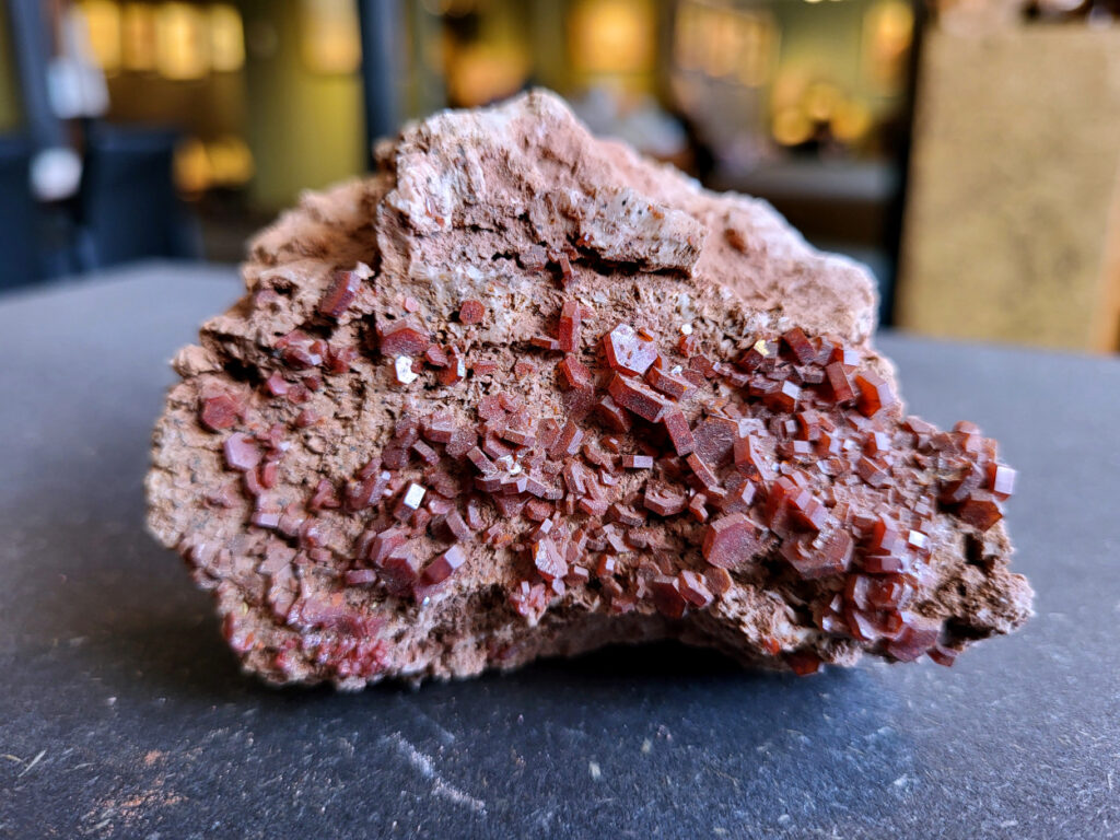 <strong>Vanadiniet, 288 gram, doorsnee 8cm, 15,- euro, nr. 105

Vanadiniet, beschrijving,

Vanadiniet is een mineraal behorend tot de groep van chlooride mineralen van lood (Pb₅(VO₄)₃Cl). Het staat bekend om zijn dieprode tot oranjerode    kristallen, vaak hexagonaal van vorm. Vanadiniet ontstaat meestal in de     oxidatiezone van loodertsen, en het wordt soms verzameld vanwege zijn spectaculaire kristalvorm en kleur. Vanadiniet kan ook geringe hoeveelheden bariet en andere achtergrondmineralen bevatten. Het heeft een hoge           densiteit en een glasachtige glans.

Associatie van Vanadiniet met Bariet
In de minerologie komt vanadiniet vaak voor op of samen met bariet, 
omdat beide mineralen zich kunnen vormen in de oxidatiezone van 
loodaders. Deze combinatie wordt soms door verzamelaars gezocht omdat de contrasterende kleuren en kristalvormen esthetisch aantrekkelijk zijn: de rode kristallen van vanadiniet op een witte of lichtgekleurde barietbasis. Van bijzondere exemplaren wordt er een hogere verzamelwaarde gegeven.
Vindplaatsen
Vanadiniet met bariet wordt gevonden in meerdere locaties wereldwijd, 
vooral in gebieden met lood- en zinkaders in woestijnachtige of rotsachtige omgevingen. Bekende vindplaatsen zijn Mexico, Marokko en sommige 
delen van de Verenigde Staten, waar vanadiniet op barietplaten in 
oxidatiezones wordt aangetroffen.

Gebruik en Verzamelwaarde
Verzamelaars: Vanadiniet-op-bariet specimens zijn populair vanwege de visuele aantrekkingskracht.
Wetenschappelijk: Beide mineralen zijn interessant voor studie van oxidatieprocessen en geochemie van zware metalen.
Industrieel: Bariet is industrieel belangrijk; vanadiniet heeft zeldzaam een kleine toepassing als vanadiumbron, maar vooral verzamelobject.
Kortom, vanadiniet op bariet is een aantrekkelijke combinatie voor mineralenverzamelaars en geeft inzicht in geologische processen in oxidatiezones van loodaders.
</strong>