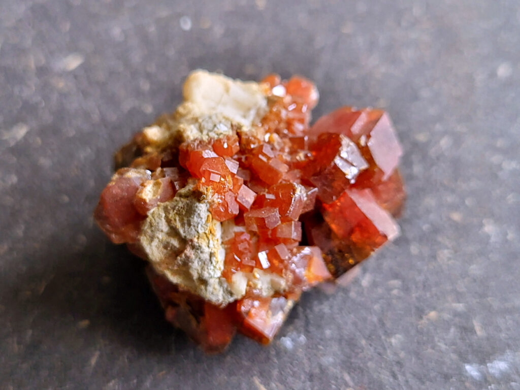 <strong>Vanadiniet, 3cm doorsnee, 12,- euro, nr. 112

Vanadiniet, beschrijving,

Vanadiniet is een mineraal behorend tot de groep van chlooride mineralen van lood (Pb₅(VO₄)₃Cl). Het staat bekend om zijn dieprode tot oranjerode    kristallen, vaak hexagonaal van vorm. Vanadiniet ontstaat meestal in de     oxidatiezone van loodertsen, en het wordt soms verzameld vanwege zijn spectaculaire kristalvorm en kleur. Vanadiniet kan ook geringe hoeveelheden bariet en andere achtergrondmineralen bevatten. Het heeft een hoge           densiteit en een glasachtige glans.

Associatie van Vanadiniet met Bariet
In de minerologie komt vanadiniet vaak voor op of samen met bariet, 
omdat beide mineralen zich kunnen vormen in de oxidatiezone van 
loodaders. Deze combinatie wordt soms door verzamelaars gezocht omdat de contrasterende kleuren en kristalvormen esthetisch aantrekkelijk zijn: de rode kristallen van vanadiniet op een witte of lichtgekleurde barietbasis. Van bijzondere exemplaren wordt er een hogere verzamelwaarde gegeven.
Vindplaatsen
Vanadiniet met bariet wordt gevonden in meerdere locaties wereldwijd, 
vooral in gebieden met lood- en zinkaders in woestijnachtige of rotsachtige omgevingen. Bekende vindplaatsen zijn Mexico, Marokko en sommige 
delen van de Verenigde Staten, waar vanadiniet op barietplaten in 
oxidatiezones wordt aangetroffen.

Gebruik en Verzamelwaarde
Verzamelaars: Vanadiniet-op-bariet specimens zijn populair vanwege de visuele aantrekkingskracht.
Wetenschappelijk: Beide mineralen zijn interessant voor studie van oxidatieprocessen en geochemie van zware metalen.
Industrieel: Bariet is industrieel belangrijk; vanadiniet heeft zeldzaam een kleine toepassing als vanadiumbron, maar vooral verzamelobject.
Kortom, vanadiniet op bariet is een aantrekkelijke combinatie voor mineralenverzamelaars en geeft inzicht in geologische processen in oxidatiezones van loodaders.
</strong>