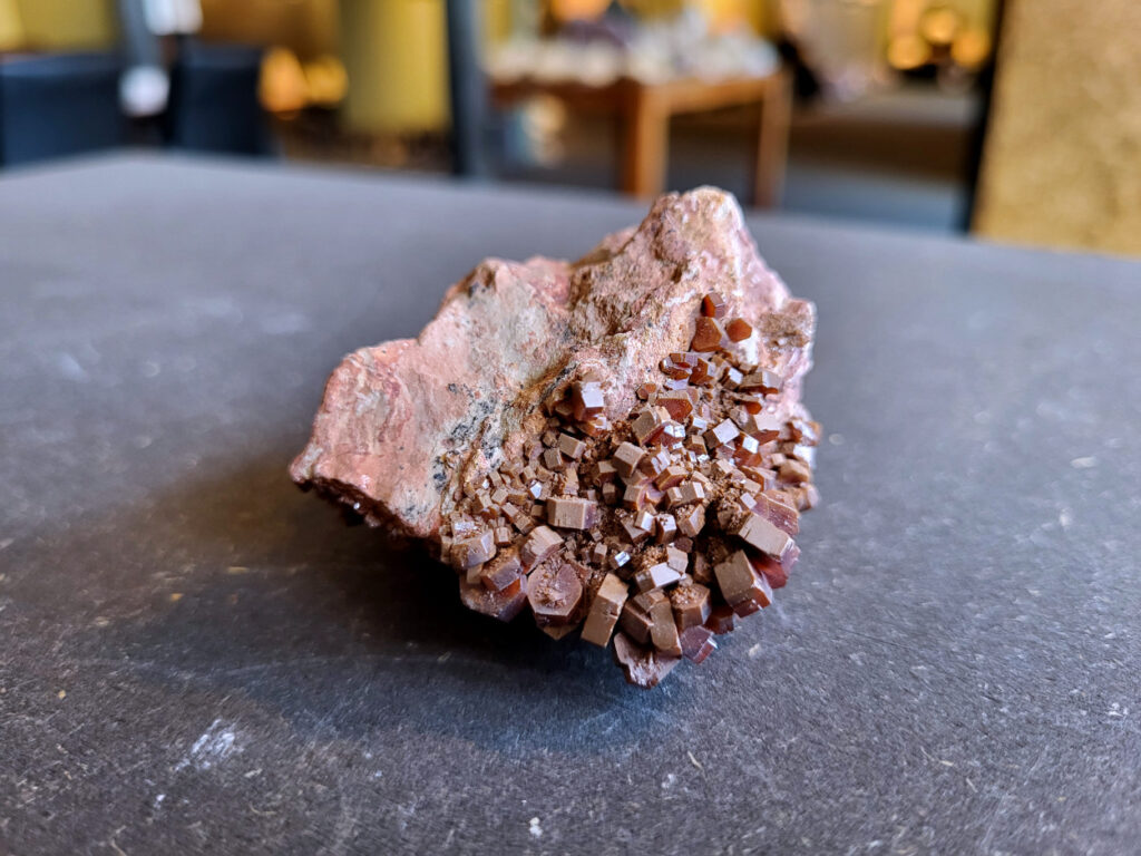 <strong>Vanadiniet op Bariet, 108 gram, doorsnee 7cm, 14,- euro, nr. 122

Vanadiniet, beschrijving,

Vanadiniet is een mineraal behorend tot de groep van chlooride mineralen van lood (Pb₅(VO₄)₃Cl). Het staat bekend om zijn dieprode tot oranjerode    kristallen, vaak hexagonaal van vorm. Vanadiniet ontstaat meestal in de     oxidatiezone van loodertsen, en het wordt soms verzameld vanwege zijn spectaculaire kristalvorm en kleur. Vanadiniet kan ook geringe hoeveelheden bariet en andere achtergrondmineralen bevatten. Het heeft een hoge           densiteit en een glasachtige glans.

Associatie van Vanadiniet met Bariet
In de minerologie komt vanadiniet vaak voor op of samen met bariet, 
omdat beide mineralen zich kunnen vormen in de oxidatiezone van 
loodaders. Deze combinatie wordt soms door verzamelaars gezocht omdat de contrasterende kleuren en kristalvormen esthetisch aantrekkelijk zijn: de rode kristallen van vanadiniet op een witte of lichtgekleurde barietbasis. Van bijzondere exemplaren wordt er een hogere verzamelwaarde gegeven.
Vindplaatsen
Vanadiniet met bariet wordt gevonden in meerdere locaties wereldwijd, 
vooral in gebieden met lood- en zinkaders in woestijnachtige of rotsachtige omgevingen. Bekende vindplaatsen zijn Mexico, Marokko en sommige 
delen van de Verenigde Staten, waar vanadiniet op barietplaten in 
oxidatiezones wordt aangetroffen.

Gebruik en Verzamelwaarde
Verzamelaars: Vanadiniet-op-bariet specimens zijn populair vanwege de visuele aantrekkingskracht.
Wetenschappelijk: Beide mineralen zijn interessant voor studie van oxidatieprocessen en geochemie van zware metalen.
Industrieel: Bariet is industrieel belangrijk; vanadiniet heeft zeldzaam een kleine toepassing als vanadiumbron, maar vooral verzamelobject.
Kortom, vanadiniet op bariet is een aantrekkelijke combinatie voor mineralenverzamelaars en geeft inzicht in geologische processen in oxidatiezones van loodaders.
</strong>