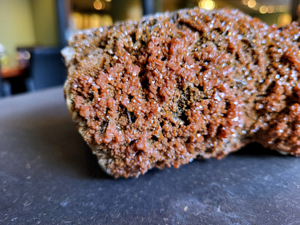 <strong>Vanadiniet op Bariet, 2,5kg, 125,- euro, detailopname, nr. 100</strong>
Vanadiniet, beschrijving,

Vanadiniet is een mineraal behorend tot de groep van chlooride mineralen van lood (Pb₅(VO₄)₃Cl). Het staat bekend om zijn dieprode tot oranjerode    kristallen, vaak hexagonaal van vorm. Vanadiniet ontstaat meestal in de     oxidatiezone van loodertsen, en het wordt soms verzameld vanwege zijn spectaculaire kristalvorm en kleur. Vanadiniet kan ook geringe hoeveelheden bariet en andere achtergrondmineralen bevatten. Het heeft een hoge           densiteit en een glasachtige glans.

<strong>Associatie van Vanadiniet met Bariet</strong>
In de minerologie komt vanadiniet vaak voor op of samen met bariet, 
omdat beide mineralen zich kunnen vormen in de oxidatiezone van 
loodaders. Deze combinatie wordt soms door verzamelaars gezocht omdat de contrasterende kleuren en kristalvormen esthetisch aantrekkelijk zijn: de rode kristallen van vanadiniet op een witte of lichtgekleurde barietbasis. Van bijzondere exemplaren wordt er een hogere verzamelwaarde gegeven.
Vindplaatsen
Vanadiniet met bariet wordt gevonden in meerdere locaties wereldwijd, 
vooral in gebieden met lood- en zinkaders in woestijnachtige of rotsachtige omgevingen. Bekende vindplaatsen zijn Mexico, Marokko en sommige 
delen van de Verenigde Staten, waar vanadiniet op barietplaten in 
oxidatiezones wordt aangetroffen.

<strong>Gebruik en Verzamelwaarde
Verzamelaars: Vanadiniet-op-bariet specimens zijn populair vanwege de visuele aantrekkingskracht.</strong>
Wetenschappelijk: Beide mineralen zijn interessant voor studie van oxidatieprocessen en geochemie van zware metalen.
Industrieel: Bariet is industrieel belangrijk; vanadiniet heeft zeldzaam een kleine toepassing als vanadiumbron, maar vooral verzamelobject.
Kortom, vanadiniet op bariet is een aantrekkelijke combinatie voor mineralenverzamelaars en geeft inzicht in geologische processen in oxidatiezones van loodaders.