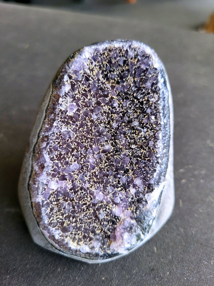 Amethist Druzy, 10 euro, nr. 2

Beschrijving Amethist.
Amethist is een paarse variëteit van kwarts, bekend om zijn kalmerende en spirituele eigenschappen. De kleur varieert van licht lila tot diep violet en wordt veroorzaakt door sporen van ijzer en andere elementen. Amethist wordt al eeuwenlang gewaardeerd, zowel vanwege zijn esthetische schoonheid als zijn vermeende genezende en beschermende krachten.
Amethist is een kwartskristal, vaak te vinden in geodes (holtes in gesteente) of als afzonderlijke kristallen.
De kleur varieert van lichtpaars tot diep violet, soms met roze of blauwe tinten.
De kleurintensiteit kan variëren, waarbij donkerdere amethisten vaak als kwalitatief worden beschouwd.
Soms vertoont amethist dichroïsme, waarbij je verschillende kleuren kunt zien wanneer je de steen in het licht draait.

Vindplaatsen:
Amethist wordt gevonden in verschillende delen van de wereld, waaronder Brazilië, Uruguay, Zambia, Madagaskar, Rusland en Canada.
Het wordt vaak gevonden in bergachtige gebieden.

Gebruik:
Amethist wordt gebruikt in sieraden, decoratieve objecten en als helende steen.
Het wordt vaak gedragen als hanger, ring of armband, of geplaatst in ruimtes om de energie te zuiveren.
Amethist wordt ook gebruikt in meditatie en andere spirituele praktijken.