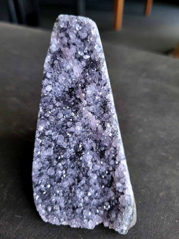 Amethist Druzy, 10 euro, nr. 3

Beschrijving Amethist.
Amethist is een paarse variëteit van kwarts, bekend om zijn kalmerende en spirituele eigenschappen. De kleur varieert van licht lila tot diep violet en wordt veroorzaakt door sporen van ijzer en andere elementen. Amethist wordt al eeuwenlang gewaardeerd, zowel vanwege zijn esthetische schoonheid als zijn vermeende genezende en beschermende krachten.
Amethist is een kwartskristal, vaak te vinden in geodes (holtes in gesteente) of als afzonderlijke kristallen.
De kleur varieert van lichtpaars tot diep violet, soms met roze of blauwe tinten.
De kleurintensiteit kan variëren, waarbij donkerdere amethisten vaak als kwalitatief worden beschouwd.
Soms vertoont amethist dichroïsme, waarbij je verschillende kleuren kunt zien wanneer je de steen in het licht draait.

Vindplaatsen:
Amethist wordt gevonden in verschillende delen van de wereld, waaronder Brazilië, Uruguay, Zambia, Madagaskar, Rusland en Canada.
Het wordt vaak gevonden in bergachtige gebieden.

Gebruik:
Amethist wordt gebruikt in sieraden, decoratieve objecten en als helende steen.
Het wordt vaak gedragen als hanger, ring of armband, of geplaatst in ruimtes om de energie te zuiveren.
Amethist wordt ook gebruikt in meditatie en andere spirituele praktijken.