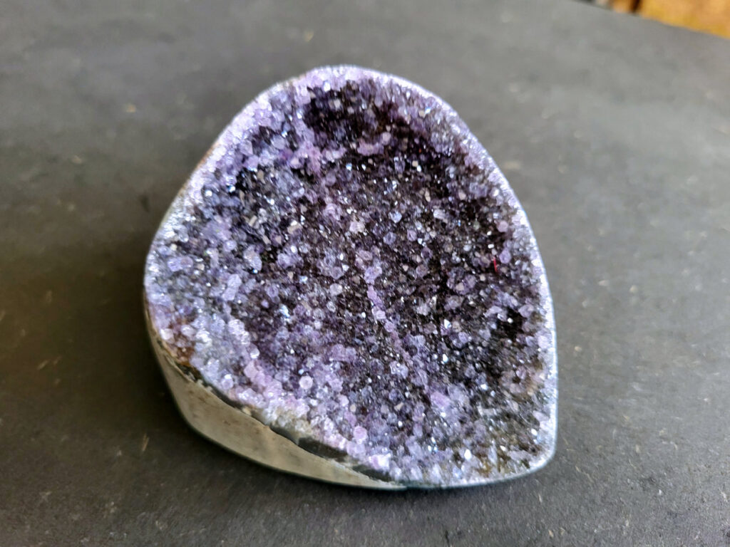 Amethist Druzy, 10 euro, nr. 4

Beschrijving Amethist.
Amethist is een paarse variëteit van kwarts, bekend om zijn kalmerende en spirituele eigenschappen. De kleur varieert van licht lila tot diep violet en wordt veroorzaakt door sporen van ijzer en andere elementen. Amethist wordt al eeuwenlang gewaardeerd, zowel vanwege zijn esthetische schoonheid als zijn vermeende genezende en beschermende krachten.
Amethist is een kwartskristal, vaak te vinden in geodes (holtes in gesteente) of als afzonderlijke kristallen.
De kleur varieert van lichtpaars tot diep violet, soms met roze of blauwe tinten.
De kleurintensiteit kan variëren, waarbij donkerdere amethisten vaak als kwalitatief worden beschouwd.
Soms vertoont amethist dichroïsme, waarbij je verschillende kleuren kunt zien wanneer je de steen in het licht draait.

Vindplaatsen:
Amethist wordt gevonden in verschillende delen van de wereld, waaronder Brazilië, Uruguay, Zambia, Madagaskar, Rusland en Canada.
Het wordt vaak gevonden in bergachtige gebieden.

Gebruik:
Amethist wordt gebruikt in sieraden, decoratieve objecten en als helende steen.
Het wordt vaak gedragen als hanger, ring of armband, of geplaatst in ruimtes om de energie te zuiveren.
Amethist wordt ook gebruikt in meditatie en andere spirituele praktijken.