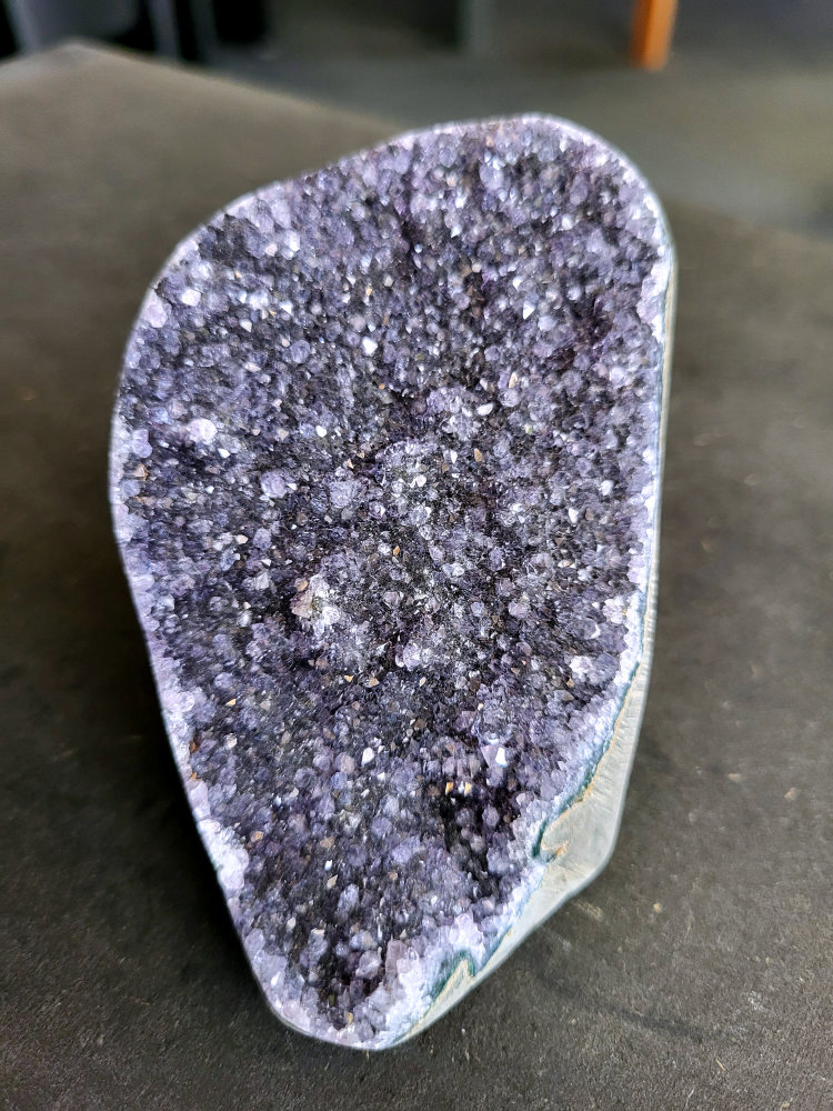Amethist druzy, 10 euro, nr. 70

Beschrijving Amethist.
Amethist is een paarse variëteit van kwarts, bekend om zijn kalmerende en spirituele eigenschappen. De kleur varieert van licht lila tot diep violet en wordt veroorzaakt door sporen van ijzer en andere elementen. Amethist wordt al eeuwenlang gewaardeerd, zowel vanwege zijn esthetische schoonheid als zijn vermeende genezende en beschermende krachten.
Amethist is een kwartskristal, vaak te vinden in geodes (holtes in gesteente) of als afzonderlijke kristallen.
De kleur varieert van lichtpaars tot diep violet, soms met roze of blauwe tinten.
De kleurintensiteit kan variëren, waarbij donkerdere amethisten vaak als kwalitatief worden beschouwd.
Soms vertoont amethist dichroïsme, waarbij je verschillende kleuren kunt zien wanneer je de steen in het licht draait.

Vindplaatsen:
Amethist wordt gevonden in verschillende delen van de wereld, waaronder Brazilië, Uruguay, Zambia, Madagaskar, Rusland en Canada.
Het wordt vaak gevonden in bergachtige gebieden.

Gebruik:
Amethist wordt gebruikt in sieraden, decoratieve objecten en als helende steen.
Het wordt vaak gedragen als hanger, ring of armband, of geplaatst in ruimtes om de energie te zuiveren.
Amethist wordt ook gebruikt in meditatie en andere spirituele praktijken.