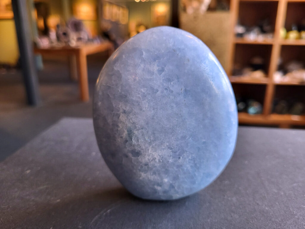 Blauwe Calciet, 10cm hoog, 10,- euro, nr. 51

Calciet, 
Calciet is een veelvoorkomend mineraal dat voornamelijk bestaat uit calciumcarbonaat. Het komt in diverse kleuren en vormen voor en wordt in veel industrieën gebruikt, maar ook in de esoterie.
Algemene kenmerken:
Samenstelling: Calciet bestaat voornamelijk uit calciumcarbonaat (CaCO3).
Vorming: Het ontstaat door afzetting van calciumcarbonaat in water, maar ook door ophoping van schelpen en skeletten van zeedieren.
Uiterlijk: Het heeft vaak een glasachtige glans, is doorzichtig tot doorschijnend en kan vele kleuren hebben, zoals geel, oranje, rood, bruin, blauw, groen, roze, wit en kleurloos.
Hardheid: Calciet heeft een hardheid van 3 op de schaal van Mohs.
Veelvoorkomend: Het is een van de meest voorkomende mineralen en is een hoofdbestanddeel van kalksteen, marmer en krijt.
Esoterie:
In de edelsteentherapie wordt calciet gezien als een steen die energie versterkt, negatieve energieën verwijdert en spirituele groei bevordert. Verschillende kleuren calciet hebben specifieke eigenschappen, zoals gele calciet voor doorzettingsvermogen en moed, en mangano calciet voor emotionele heling.
Specifieke calcietsoorten:
Gele Calciet: Staat bekend om het absorberen van negativiteit, het versterken van doorzettingsvermogen en het aantrekken van succes.
Blauwe Calciet: Wordt geassocieerd met kalmering, communicatie en het loslaten van stress.
Groene Calciet: Werkt op de hartchakra, bevordert liefde, compassie en emotionele heling.
Mangano Calciet: Wordt gebruikt voor emotionele heling, het loslaten van oud verdriet en het versterken van zelfvertrouwen.
Reiniging:
Calciet kan op verschillende manieren gereinigd worden, maar het is belangrijk om te weten dat sommige soorten, zoals gele calciet, niet goed tegen water kunnen.
Andere reinigingsmethoden zijn bijvoorbeeld reinigen met edelstenenspray, op een Amethist of bergkristal leggen, of reinigen met selenite.
Het is een steen die kan worden gebruikt voor energieversterking, emotionele heling en het bevorderen van spirituele groei, afhankelijk van de specifieke kleur en eigenschappen.
-Kunstgalerie Arnold-