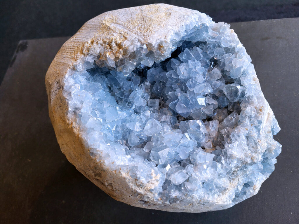 Celestien, 5,8kg, doorsnee 24cm, 145,- euro, nr. 520

Celestien,
Celestien, ook wel bekend als celestiet of Coelestien, is een mineraal dat voornamelijk bestaat uit strontiumsulfaat. De naam is afgeleid van het Latijnse "coelestis", wat "hemels" betekent, vanwege de vaak blauwachtige kleur. Celestien staat bekend om zijn kalmerende en relativerende werking en wordt vaak geassocieerd met engelen en spirituele ontwikkeling.
Eigenschappen en kenmerken:
Kleur: Celestien kan kleurloos, wit, grijs, blauw, groen, geel, oranje, roodachtig of bruin zijn, maar de meest voorkomende kleur is grijsblauw.
Vorm: Het komt voor als tabulaire of prismatische kristallen, vezels en massa's.
Hardheid: De hardheid van celestien is 3 tot 3,5 op de hardheidsschaal van Mohs.
Glans: Het heeft een glasachtige glans en is vaak doorzichtig tot doorschijnend.
Herkomst: Het mineraal wordt gevonden in graniet en pegmatiet, en ook gevormd bij het verdampen van zeewater.
Spirituele betekenis en werking:
Kalmerend en ontspannend:
Celestien staat bekend om zijn kalmerende werking en wordt vaak gebruikt om stress, angst en nervositeit te verminderen.
Spirituele ontwikkeling:
De steen bevordert spirituele groei, helderziendheid en telepathie.
Engelensteen:
Celestien wordt vaak geassocieerd met engelen en wordt gebruikt om contact te leggen met engelen en gidsen tijdens meditatie en dromen.
Bevordert focus en concentratie:
Celestien kan helpen bij het verbeteren van focus, concentratie en het begrijpen van teksten.
Verbinding met de keel, voorhoofd en kruinchakra:
De steen richt zich voornamelijk op het keelchakra, voorhoofdschakra en kruinchakra.
Fysieke werking:
Pijnstillend: Celestien kan kalmerend werken en pijn verminderen, inclusief menstruatiepijn.
Helpt bij oog- en oorproblemen: De steen kan behulpzaam zijn bij kwalen aan ogen en oren.
Geeft energie bij vermoeidheid: Celestien kan energie geven bij uitputting en vermoeidheid.
Bevordert genezing: De steen zou kunnen helpen bij de genezing van botten, weefsels en organen.
Verzorging:
Celestien is een gevoelige steen en kan beschadigen door water of zout.
Reinig de steen met zachte methoden zoals rook van witte salie of palo santo.
Laad de steen op in een amethist cluster, seleniet of in maanlicht.
Vermijd fel zonlicht, omdat dit de kleur van de steen kan doen vervagen.