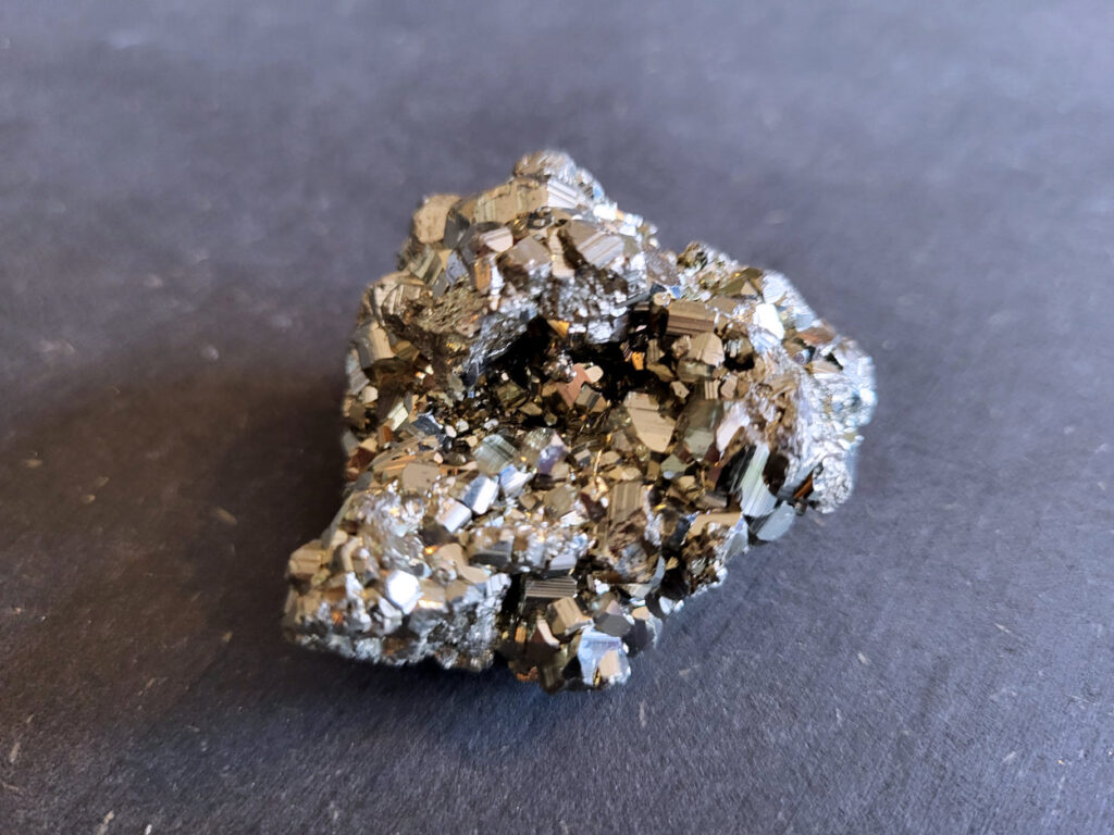 Pyriet, tussen 3,- en 6,- euro, nr. 6

Pyriet, beschrijving
Pyriet, ook wel bekend als klatergoud. Het is een mineraal van ijzer en zwavel met een goudgele, metaalachtige glans, wat het soms doet lijken op goud. De naam komt van het Griekse woord voor 'vuur' ,
omdat het vonken geeft als je het ergens tegenaan slaat. Het wordt industrieel gebruikt voor de productie van zwavelzuur en als decoratieve steen, terwijl het in de oudheid diende als vuursteen.
Kenmerken
Uiterlijk: Goudgeel met een metaalachtige glans. De kristallen zijn vaak kubusvormig, maar kunnen ook andere vormen hebben.
Naam: Afgeleid van het Griekse woord voor 'vuur', vanwege het vonkend effect bij impact.
Bijnaam: Ook wel "klatergoud" of "goud der dwazen" genoemd vanwege de gelijkenis met echt goud.
Toepassingen en gebruik
Industrie: Het is een belangrijke bron voor de productie van zwavelzuur, dat onder andere wordt gebruikt in kunstmest en olieraffinage.
Geschiedenis: In de oudheid werd het gebruikt als vuursteen om vuur te maken.
Decoratie en sieraden: Vanwege zijn goudachtige uiterlijk wordt het veel gebruikt in sieraden en decoratieve objecten.
Wetenschap: Het dient als indicator voor geologische processen en wordt gebruikt in mineralogisch onderzoek.
Onderscheid met goud
Textuur: Ruwe pyrietkristallen hebben scherpere randen dan ruw goud.
Kleur: Pyriet heeft vaker een koperachtige tint, terwijl echt goud een helderder, geelgouden kleur heeft.
Hardheid: Pyriet is harder dan goud (hardheid van 6-6,5 versus 2,5).
Dichtheid: Pyriet is lichter in gewicht dan goud.